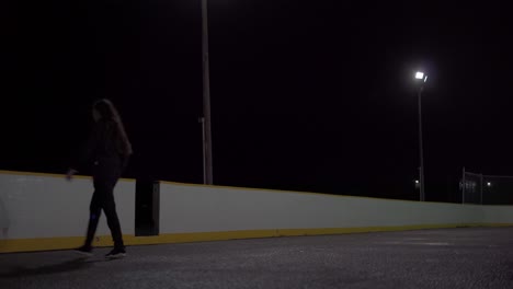 tiro estático de ángulo bajo de una adolescente tomando tiros en una red de baloncesto en una cancha al aire libre por la noche