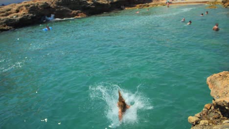 Cámara-Lenta-De-Una-Turista-En-Traje-De-Baño-Salta-Desde-El-Borde-Rocoso-Al-Mar-En-Verano