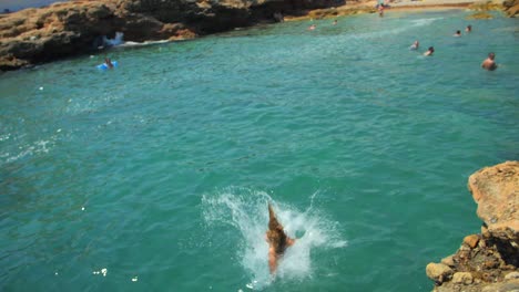slow motion of a female tourist in swimwear jumps from the rocky edge into sea in summer