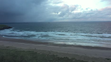 Aerial-view-of-cargo-ships-on-the-Atlantic-ocean-and-a-beach,-dark,-moody-evening---pan,-drone-shot