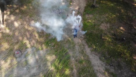 Toma-Aérea-De-Un-Hombre-Jugando-Con-Dos-Bombas-De-Humo-Blanco-En-La-Naturaleza