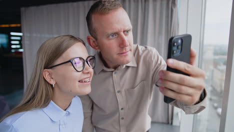 man and woman in office looking at the phone. male colleague takes female's glasses to see better something on his phone. close up.