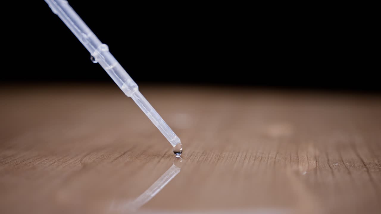 Water drop falling from a pipette, close-up view with a smooth wooden surface