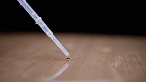 water drop falling from a pipette, close-up view with a smooth wooden surface