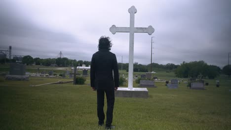 young, religious man in black suit worshipping and praying in front of christian cross