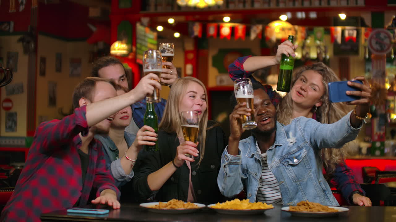 Un gruppo di amici eterogenei si fa un selfie con il cellulare in un bar.