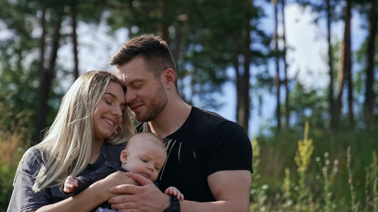 Happy sitting couple hold their newborn baby. Loving couple spending happy time together in nature in summer.