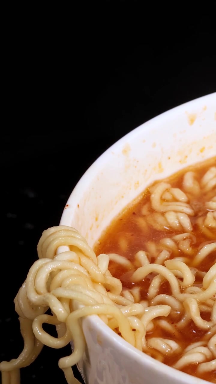 ドラマチックな照明の下、白い丼の中で辛い赤いスープが飛び散るインスタントラーメンのクローズアップ。