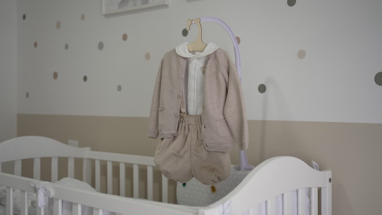 Neutral baby clothes hang above crib in soft pastel nursery interior