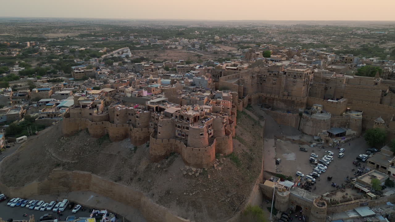 una toma de avión no tripulado hacia atrás del fuerte de jaisalmer al atardecer, mostrando la arquitectura de piedra arenisca dorada y el paisaje urbano de rajasthan, india con el caloroso resplandor del sol poniente