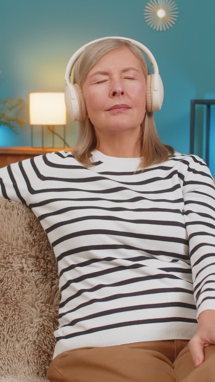 Mature woman relaxing resting with calm music sitting on sofa with headphones eyes closed at home