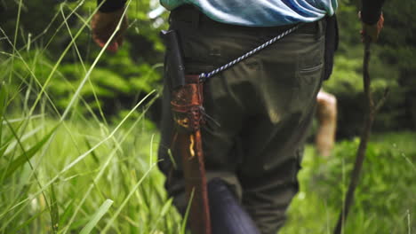 close up of male walking in a forest with machete big sharp knife and a wooden stick