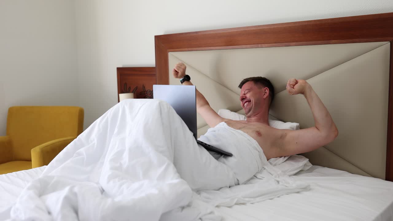 Man in bed with laptop celebrating success