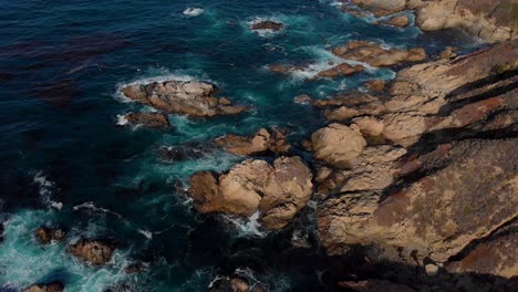 Slow-pan-up-over-beautiful-water-crashing-over-rocky-coastline-during-sunset