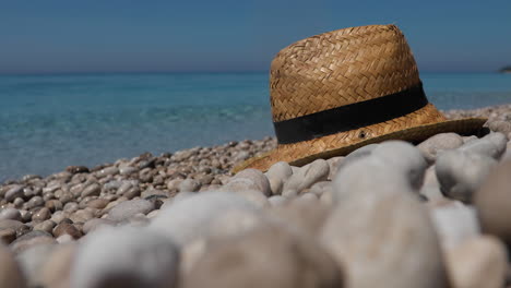 Hat-thrown-over-pebbles-on-beach-washed-by-blue-crystal-sea-water,-summer-vacation