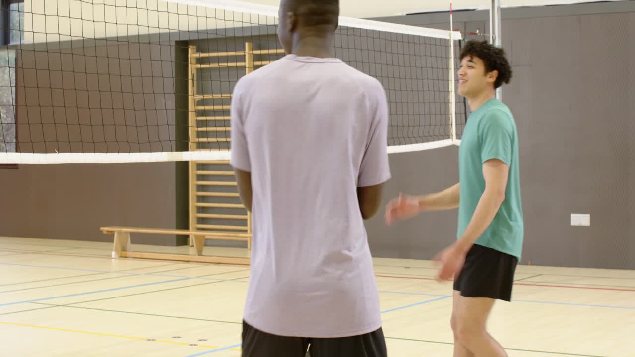 Diverse male teammates following Player A with volleyball, moving to net in gym preparing to serve