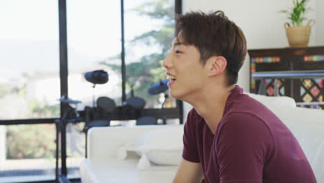 happy asian male teenager watching tv and sitting in living room