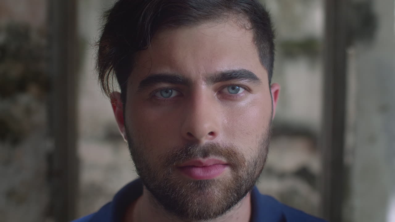 High-quality 4K footage of a focused young man with blue eyes and a beard, slowly opening his eyes in a cinematic outdoor setting. Ideal for travel, identity, mystery, or emotional