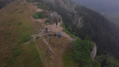 aerial helix drone shot of three hikers on a mountain summit near a steep cliff