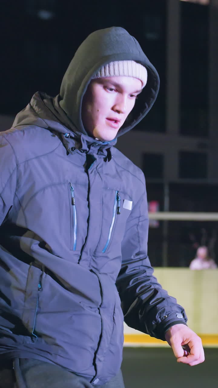 Side view of footballer joggling football skillfully during nighttime practice on urban sports field, illuminated by streetlights, against a backdrop of tall building