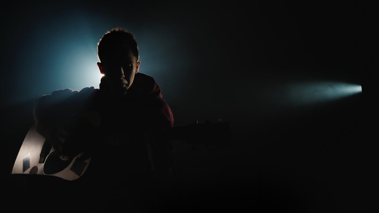 un joven toca la guitarra sentado en el escenario 1