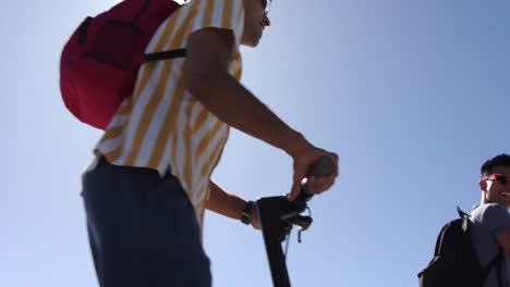 happy diverse gay male couple using scooters at promenade by the sea, slow motion