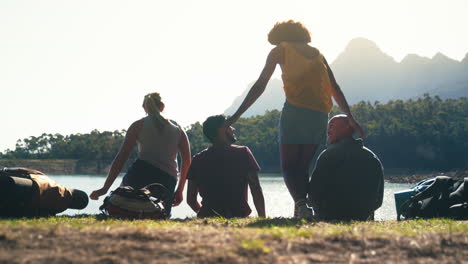 Rear-View-Group-Of-Friends-On-Vacation-Hiking-Sitting-And-Looking-At-Lake-And-Mountains