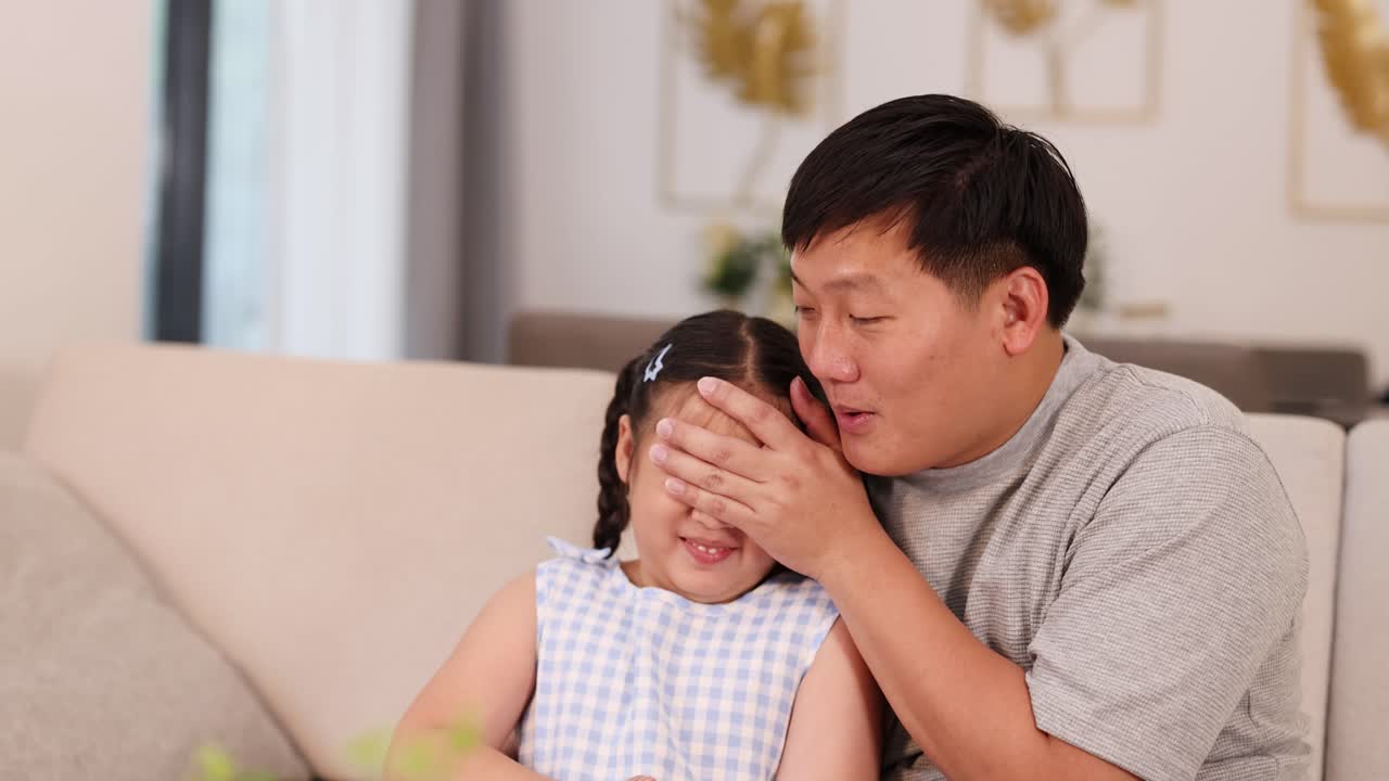 A father and daughter enjoy a playful, intimate moment on a cozy sofa in a warmly lit living room