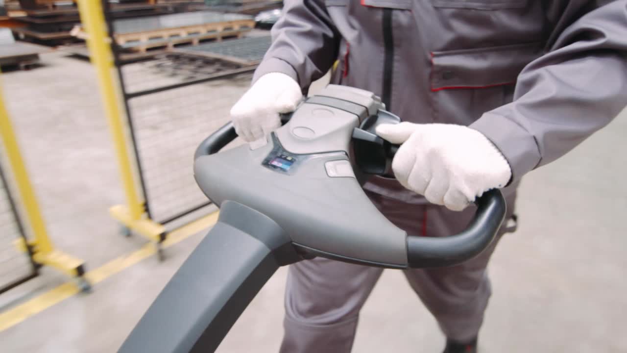 Warehouse worker's hands drive hand pallet truck close up