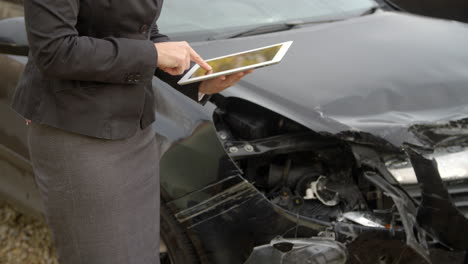 loss adjuster with digital tablet inspecting damaged car