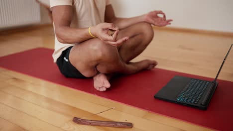 él pega sus dedos juntos y medita en frente de la computadora portátil con palillo de aroma