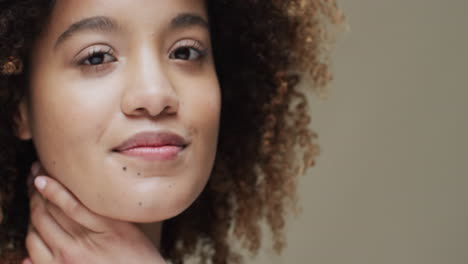 mujer feliz de dos razas con cabello oscuro tocando el cuello sobre un fondo beige, cámara lenta