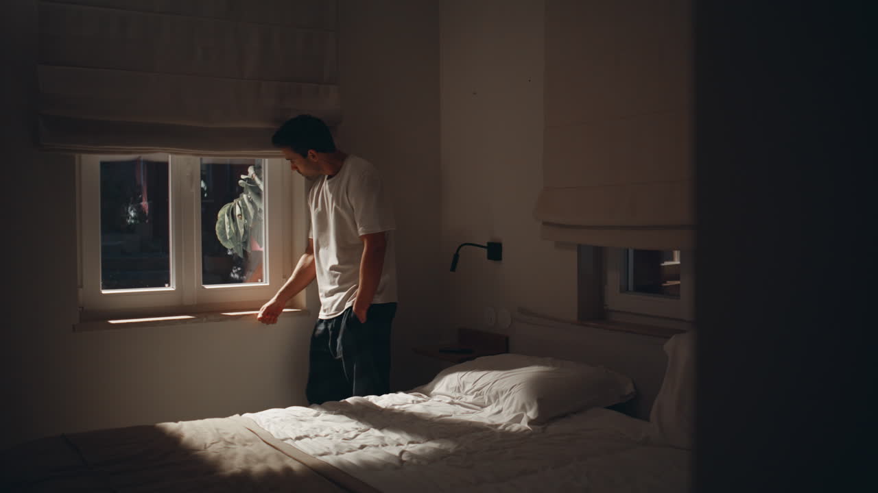 Sorrowful guy standing night bedroom looking dark window. Restless man at home