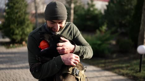 un hombre jugando en el patio de la casa con un perro de servicio en collar de protección militar y acariciarlo