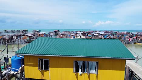 close-up drone shot of a unique yellow water house with sea skyline and houses background, at borneo - pulau omadal, sabah, malaysia