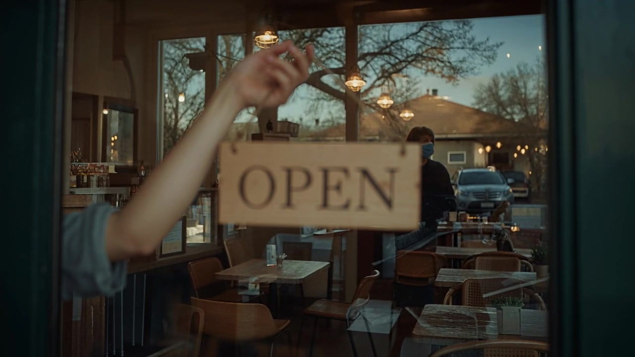 Reaching forearm wearing rolled-up sleeve, holding OPEN sign on cafe glass door, signaling open