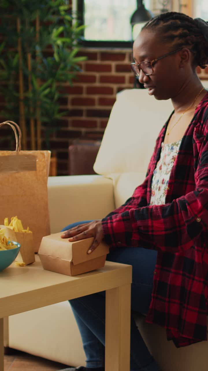 Vertical video: Young adult taking out hamburger and fries