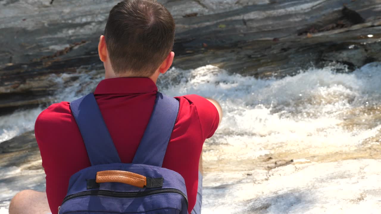 산강 근처에 앉아 있는 배을 들고 있는 평범한 젊은이, 거리는 강을 바라보는 남자 여행자, 더 많은 여행을 꿈꾸는 남자, 신선한 공기와 자연의 아름다움을 즐기는 남자, 활동적인 생활 방식과 여행의 개념.
