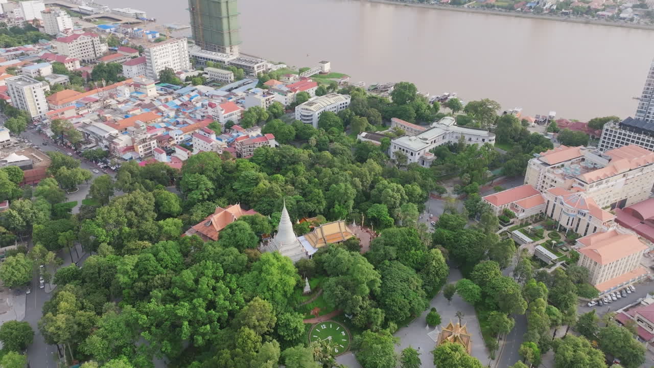 Bird’s-eye view of Wat Phnom temple surrounded by dense trees and curved roads with the river in the background