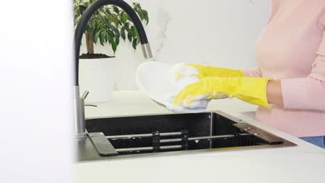 a young woman wearing yellow protective gloves washes dishes at the kitchen sink