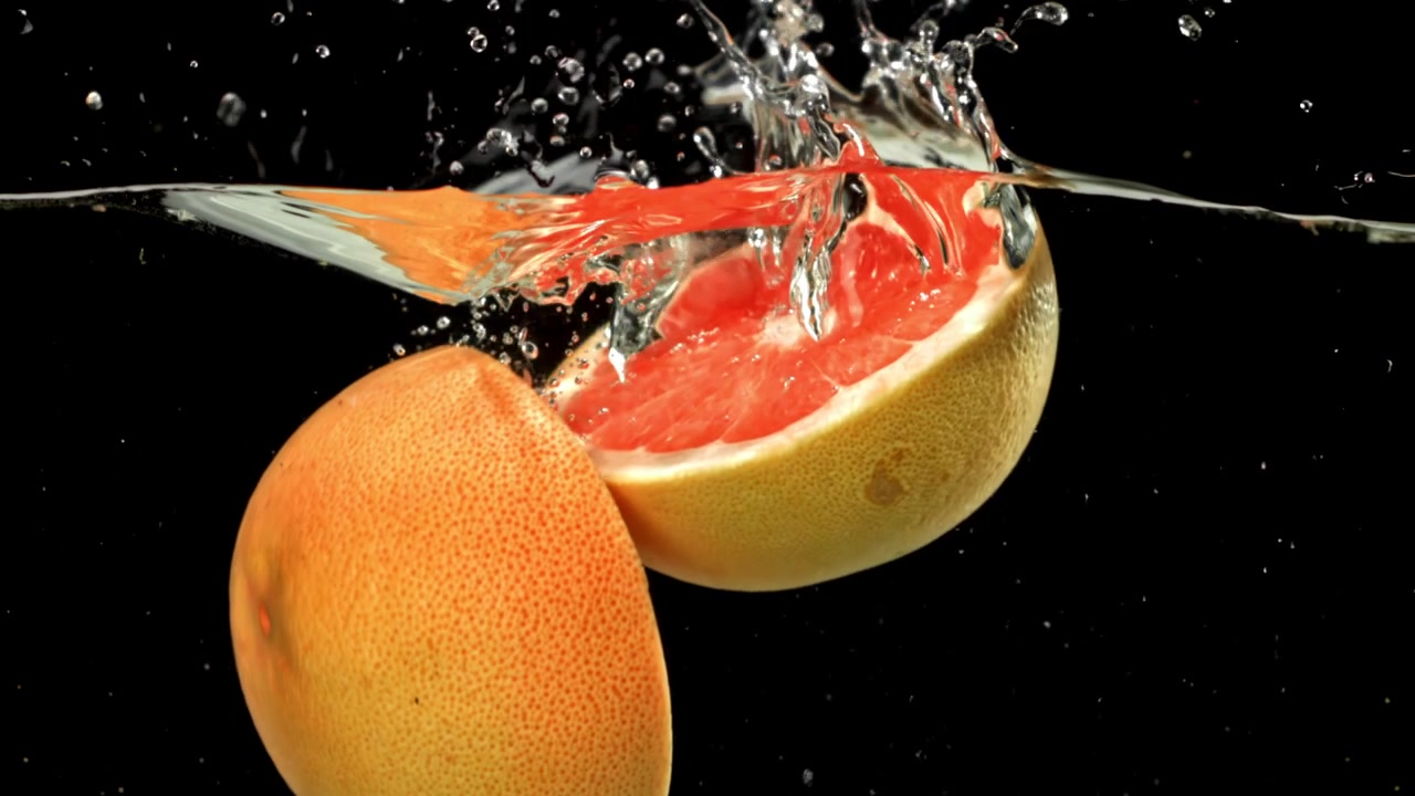 Pompelmo fresco tagliato a metà che si tuffa nell'acqua con uno schizzo al rallentatore