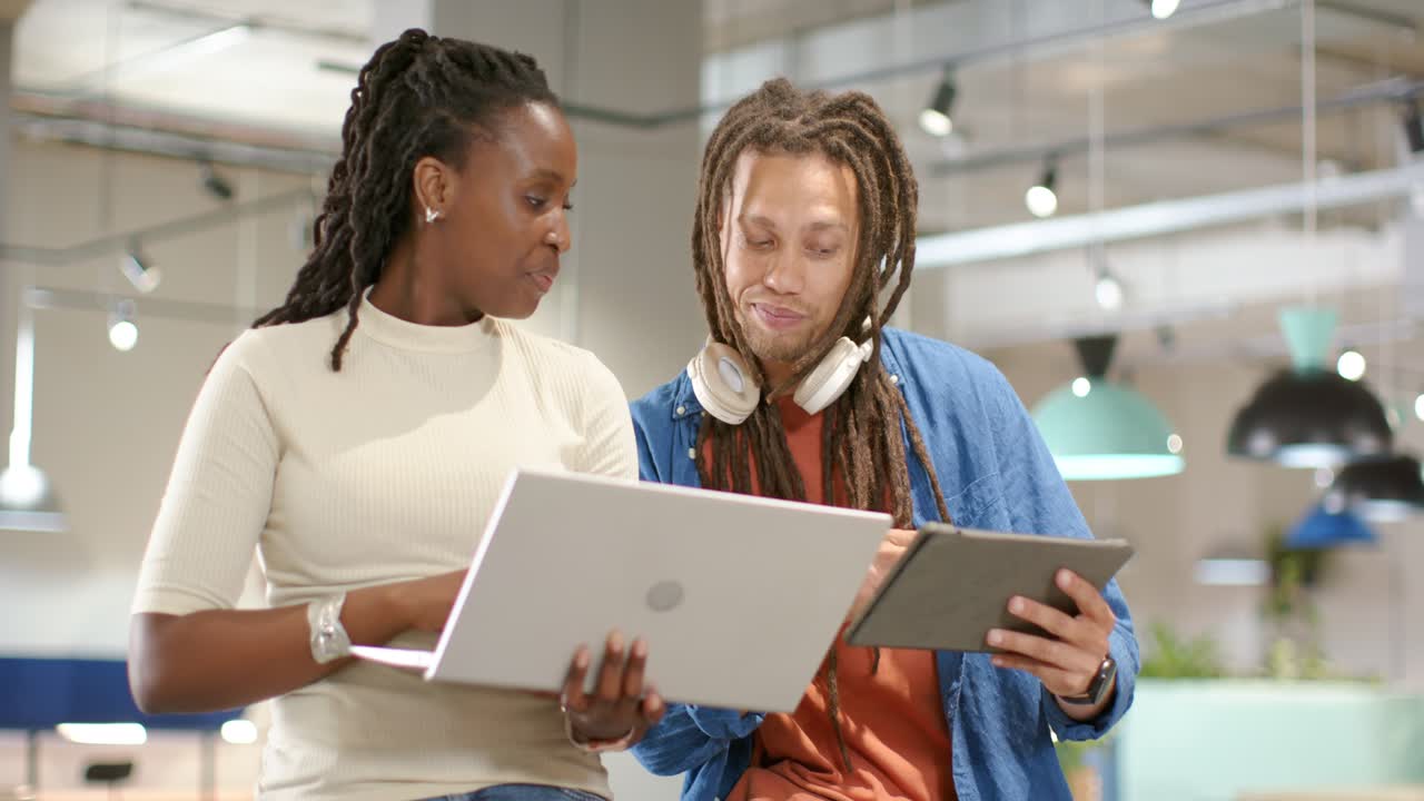 African American coworkers at office woman presenting laptop, man pointing tablet, checking data