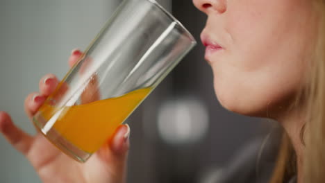 close up view of woman holding transparent glass while drinking orange juice, soft bokeh background adds a warm, cozy ambiance, refreshing scene emphasizes hydration