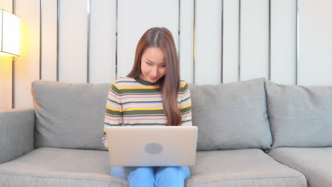 Eine-Junge-Frau,-Die-Auf-Einer-Couch-Sitzt,-Arbeitet-Erfolgreich-An-Ihrem-Laptop