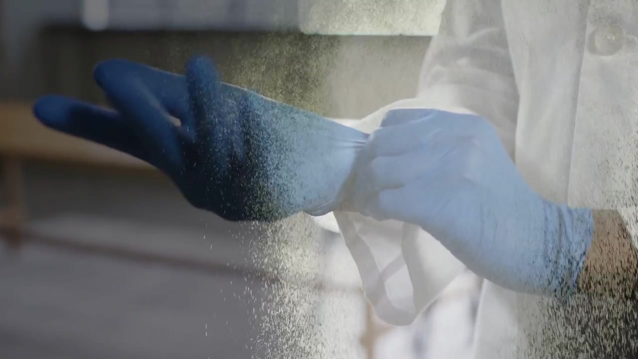 Lab worker in white coat donning blue gloves for sterile procedure, spray appearing over hands
