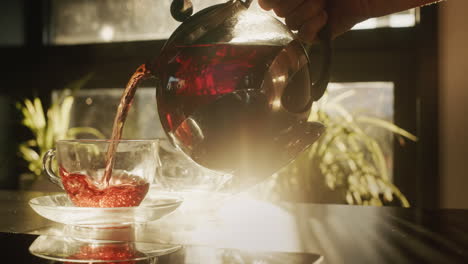 pouring tea from a teapot into a glass cup. the sun shines from the window, beautifully illuminates the dishes