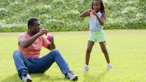african american, father and daughter blowing bubbles together on grass, enjoying playful outdoor fu