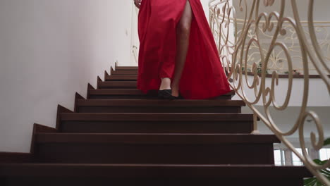 elegant woman gracefully descends staircase. young woman ready for romantic date wearing red cocktail dress to make impression. radiant presence in residence