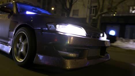 modified car driving at night in a city street with snow