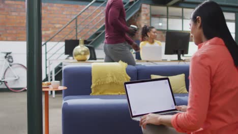 mujer de negocios biracial feliz usando una computadora portátil con espacio de copia en la oficina